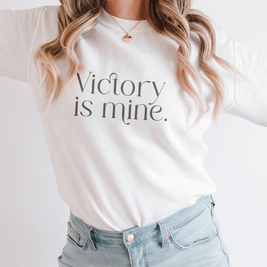 Blonde woman wearing a white Christian sweatshirt with "Victory is Mine" message in modern serif font, symbolizing faith and strength in a minimalist design