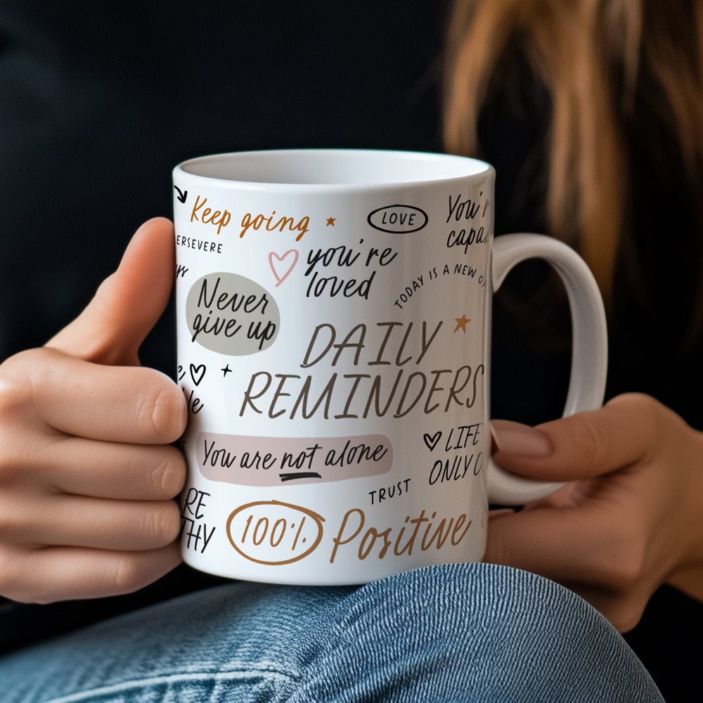 Hands holding a daily reminders mug with positive affirmations in handwritten fonts, decorated with delicate illustrations