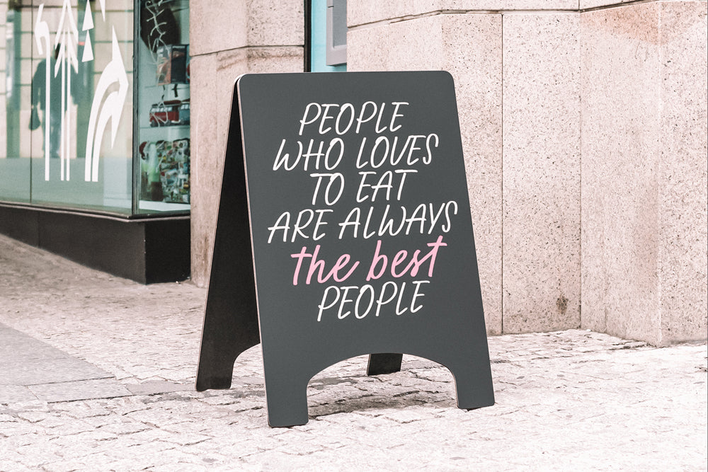 Blackboard sign on a sidewalk with the quote "People who love to eat are always the best people" in handwritten script font