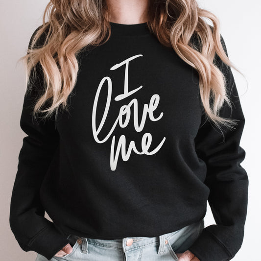 Blonde woman wearing a black "I love me" sweatshirt with modern script lettering, promoting self-love and confidence in a chic, minimalist style