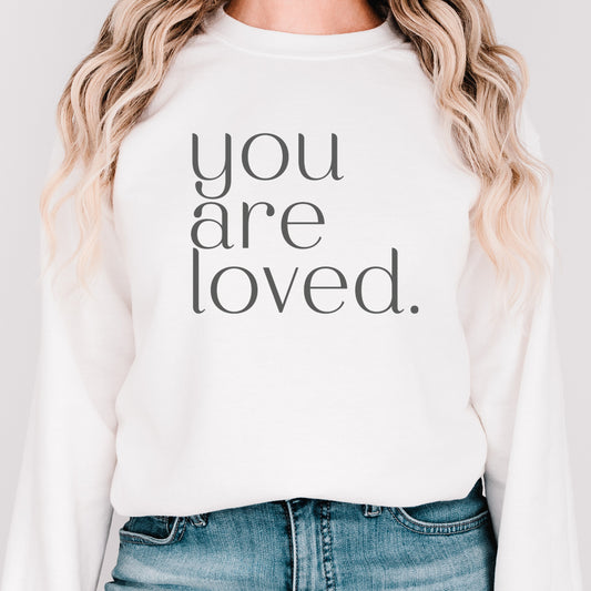 Blonde woman wearing a white "you are loved" sweatshirt with modern serif font, promoting love in a chic, minimalist style